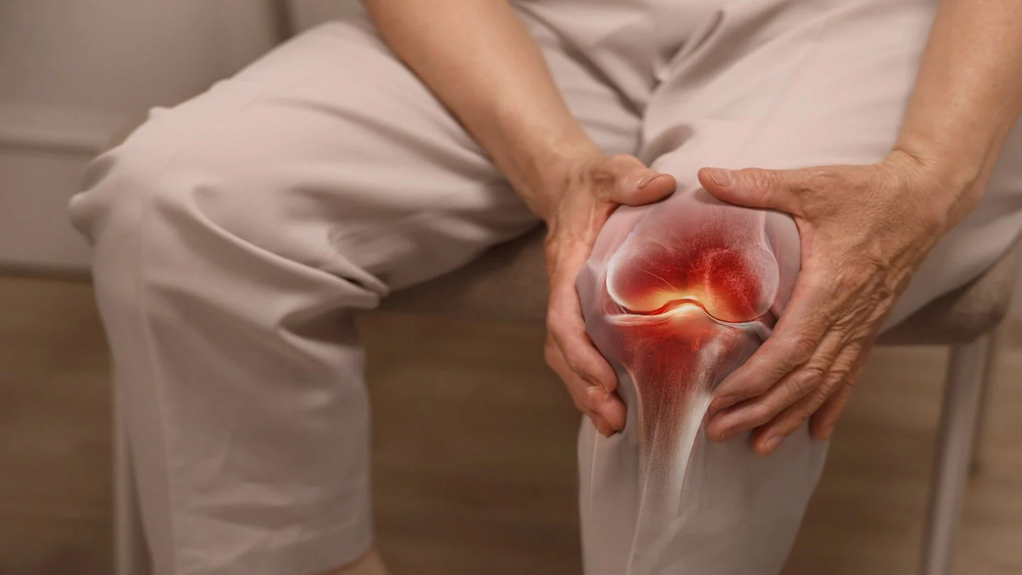 An older adult sitting and holding their knee in pain, with a digital illustration showing inflammation and discomfort inside the knee joint.